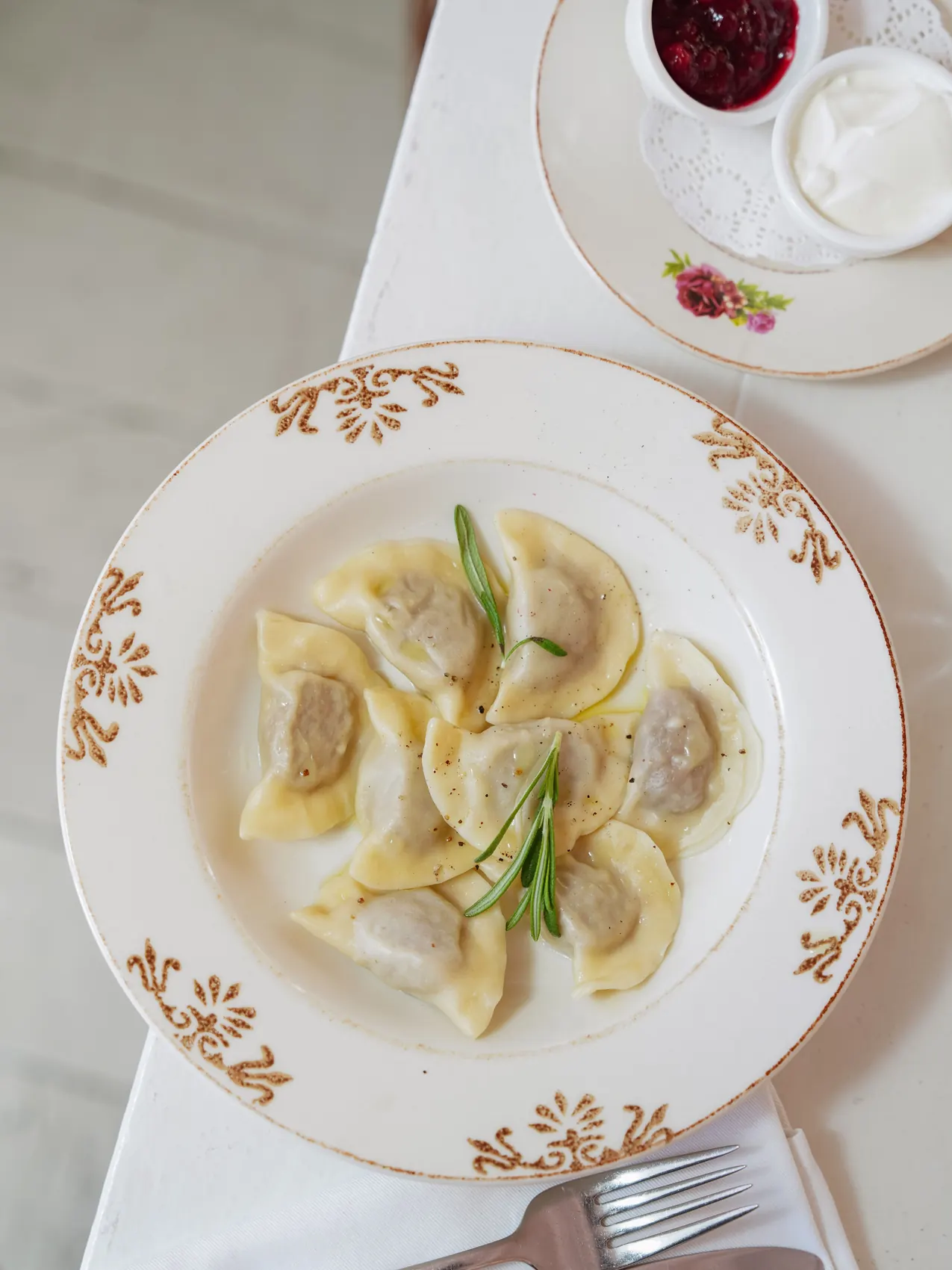 Top view of boiled Polish pierogi dumplings on a decorative plate with sour cream and berry jam, garnished with rosemary