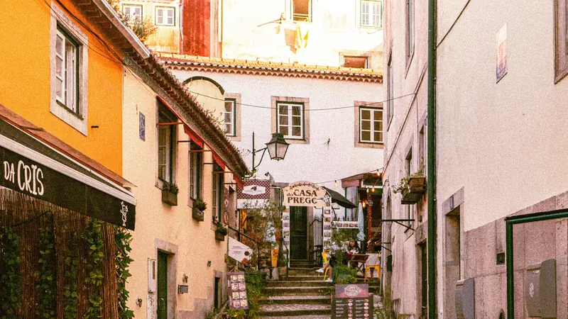 Narrow historic street in Lisbon with colourful buildings, stone steps, and small local restaurants