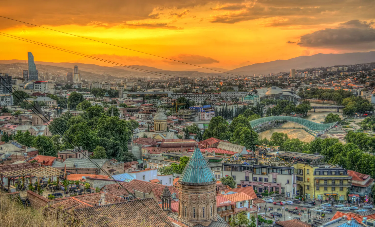Sunset over Tbilisi in summer with the iconic Bridge of Peace arching over the Mtkvari River.