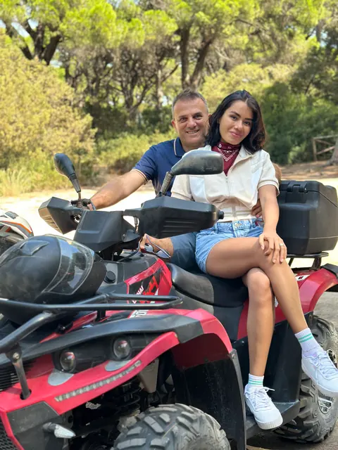 Smiling couple sitting together on a red quad bike in a pine forest