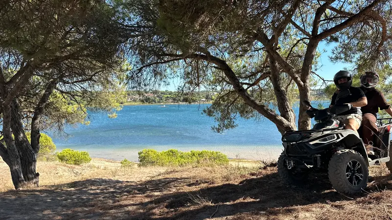 Two people enjoying an exciting ATV ride surrounded by rugged scenery, with stunning crystal-blue waters creating a beautiful backdrop behind them.