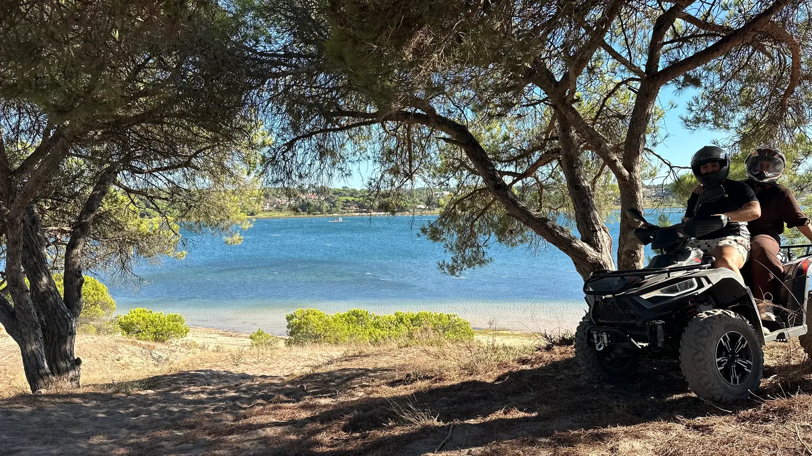 Two people enjoying an exciting ATV ride surrounded by rugged scenery, with stunning crystal-blue waters creating a beautiful backdrop behind them.
