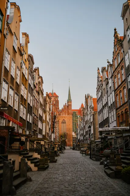 Cobblestone street lined with historic colorful buildings in Gdańsk Main Town with St. Mary’s Basilica spire visible in the distance