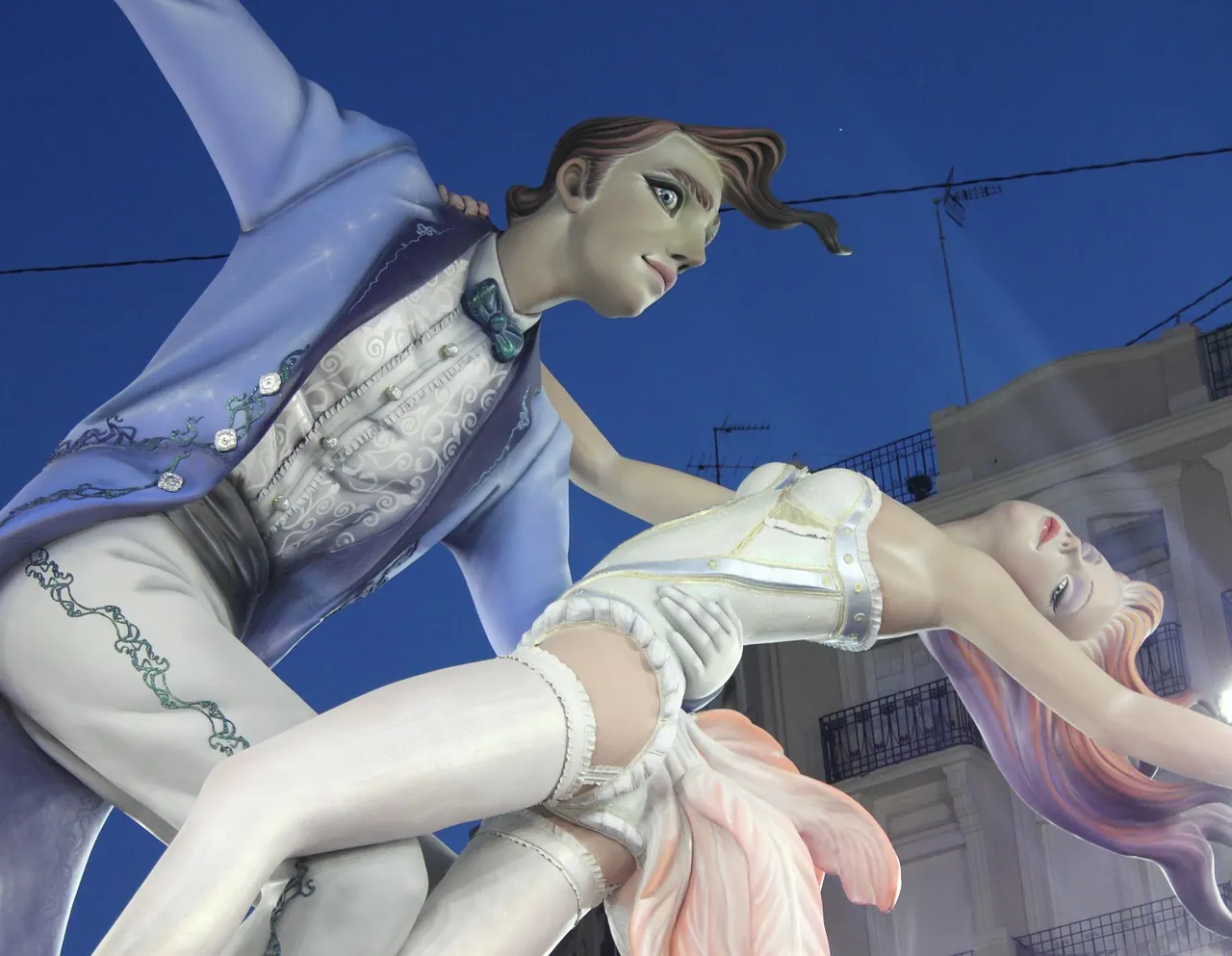 Two colorful sculptures of a couple in a dance pose against a deep blue sky, with elegant clothing and expressive features, creating a whimsical mood.