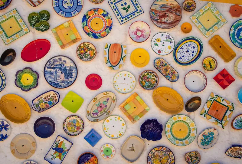 Colorful handcrafted ceramic plates with intricate patterns arranged on a white wall background. Vibrant designs evoke a cheerful mood.