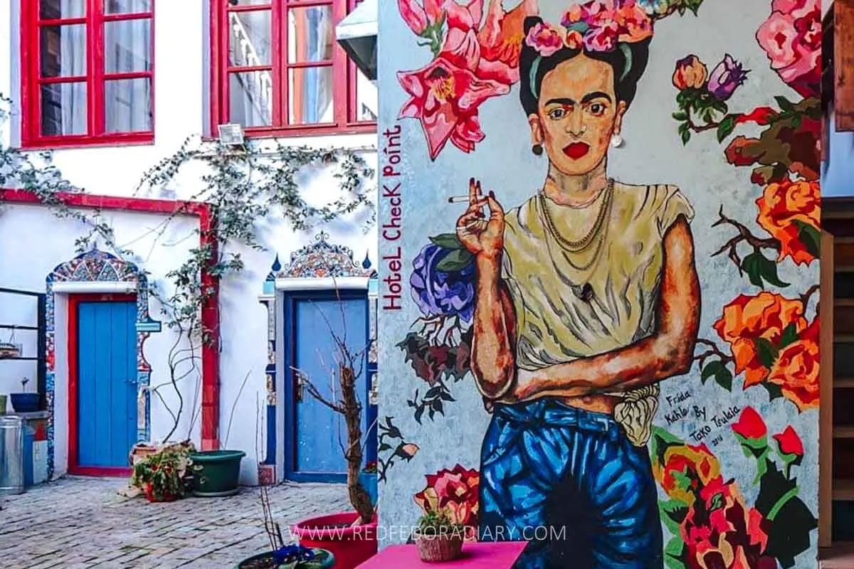 Vibrant street art in Tbilisi showcases a colorful mural of a famous artist, surrounded by floral elements, adding creativity and charm to the hotel's courtyard setting.