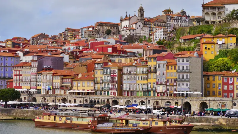 Colorful historic buildings of the Ribeira district along the Douro River in Porto, Portugal with traditional boats docked at the waterfront.