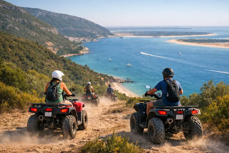 ATV riders descend a dusty hillside trail above a blue bay and sandy coast, with boats in the water below.