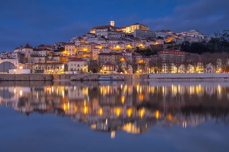 Coimbra, a city of timeless beauty and academic prestige, reveals its most enchanting side as day turns to night. Perched majestically on a hill, the city’s ancient buildings ignite with a warm, golden glow, creating a