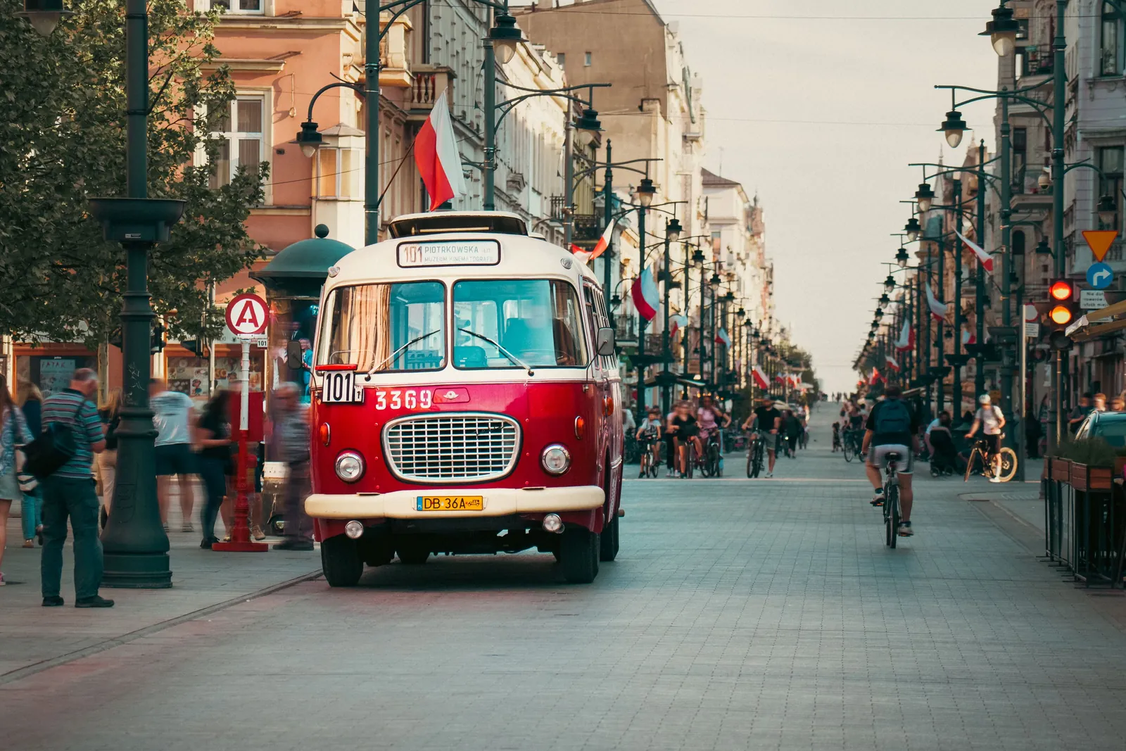 Vintage red-and-white tram marked 101/Piotrkowska rolls down a busy city street with cyclists, pedestrians, and Polish flags.